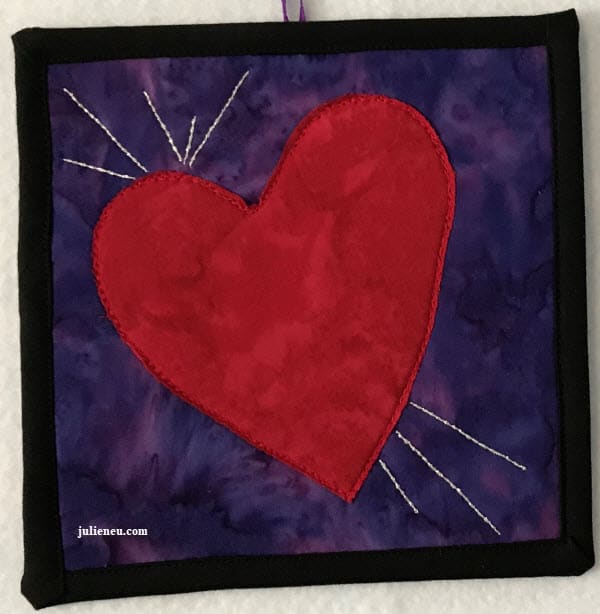 Small quilted art piece reflecting "joy". Red heart on purple background with silver thread lines emanating from heart on left lobe and bottom.