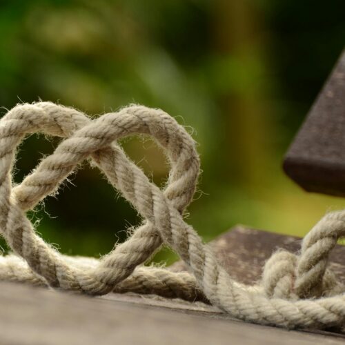 brown rope tangled and formed into heart shape on brown wooden rail