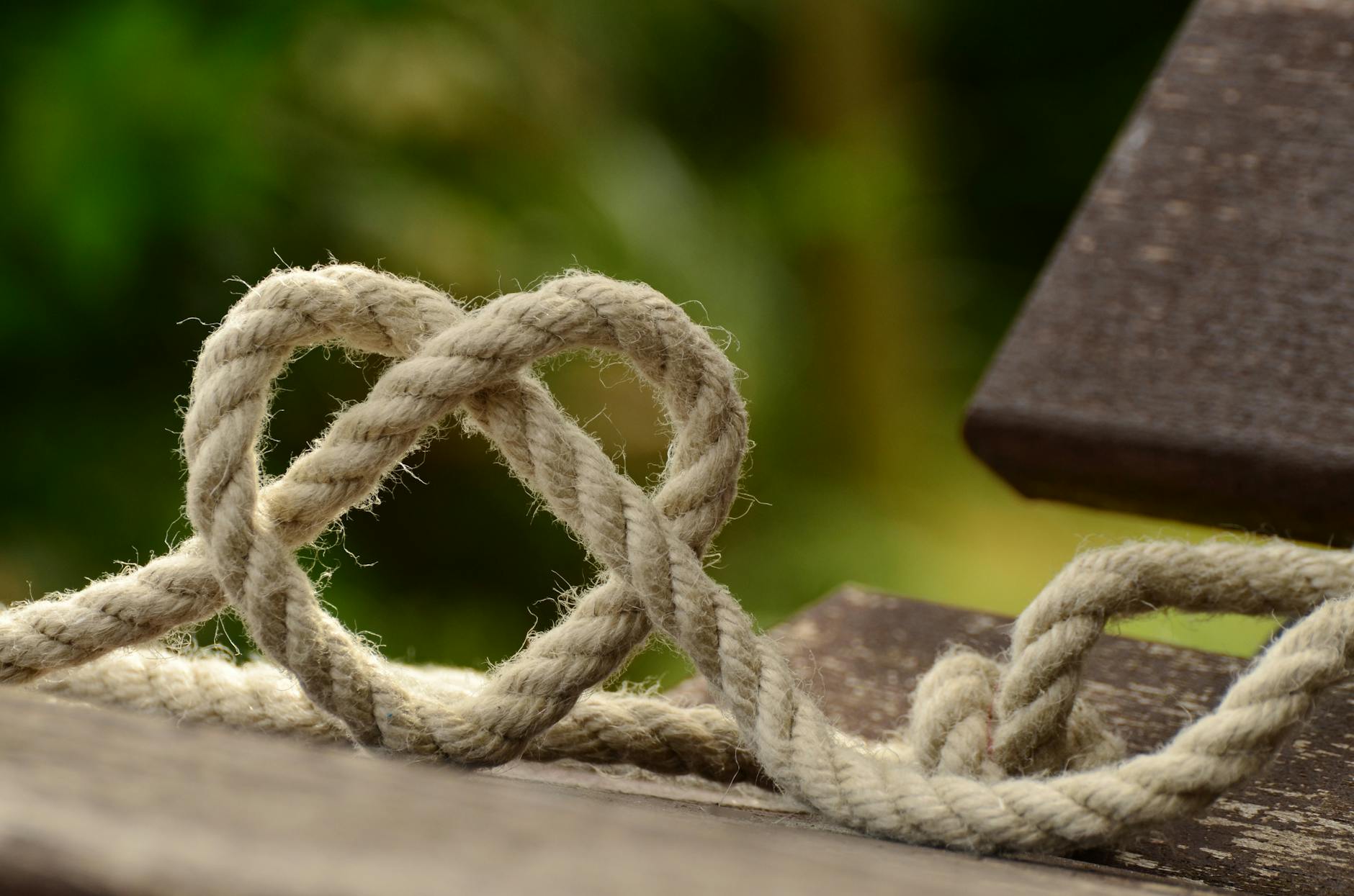 brown rope tangled and formed into heart shape on brown wooden rail